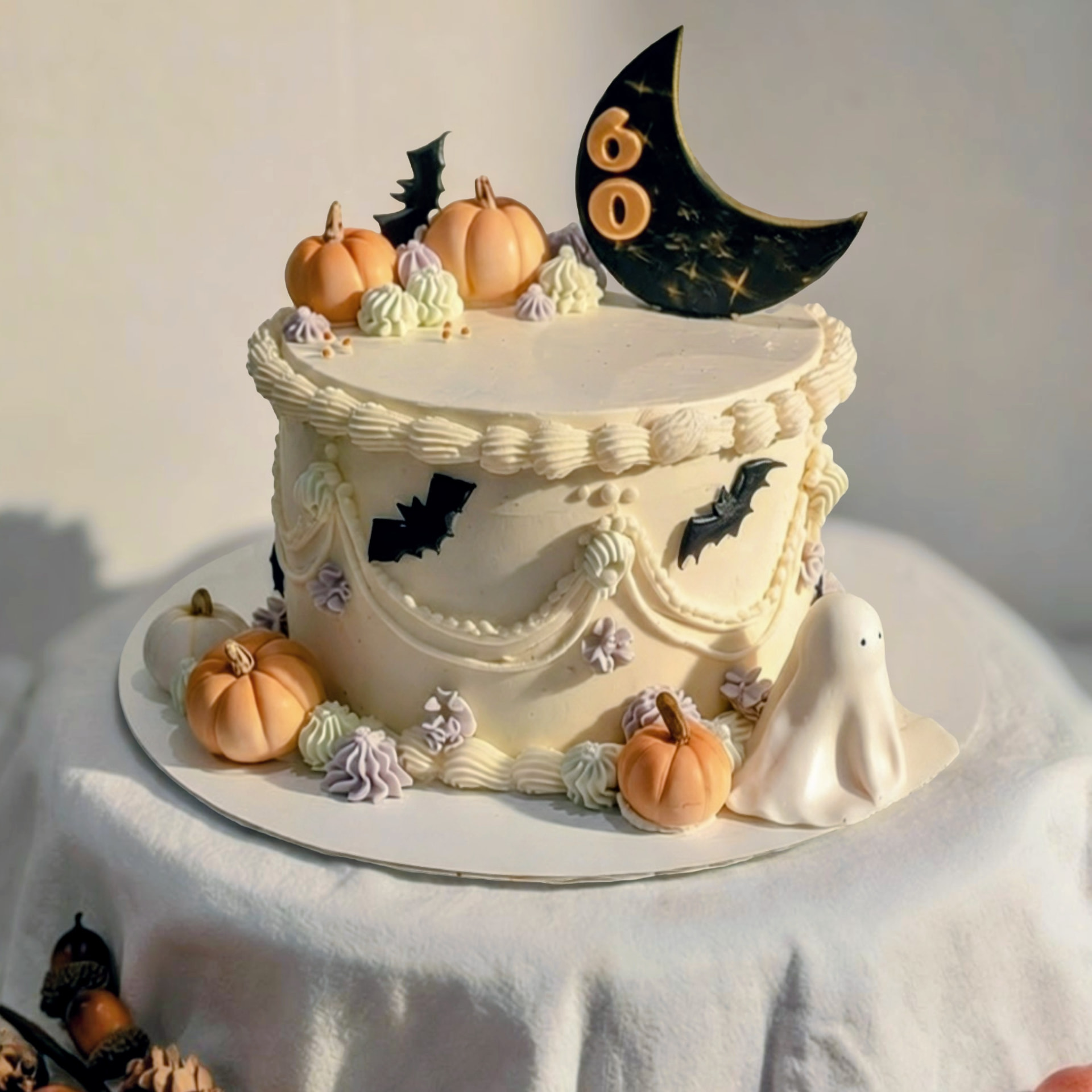 Halloween 60th birthday cake with ivory buttercream and lambeth-style piping, a black crescent moon topper marked 60, piped pumpkins, bats, and a white ghost figurine