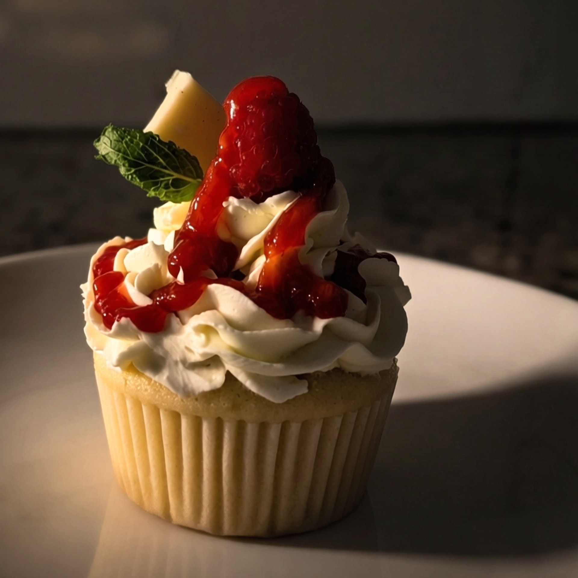 Vanilla cupcake filled with fresh raspberry compote, topped with a fresh raspberry, white chocolate, and a mint leaf