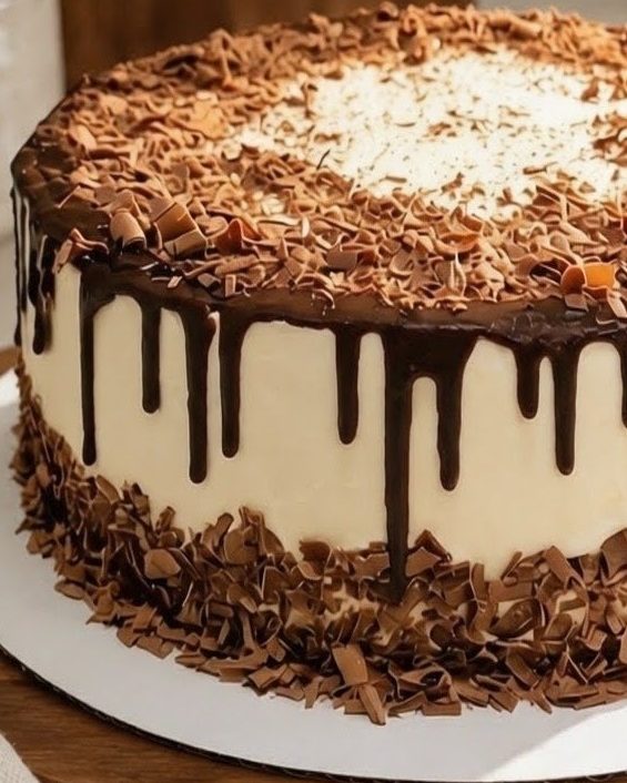 Chocolate drip layer cake with chocolate shavings on top and a border of chocolate curls around the base